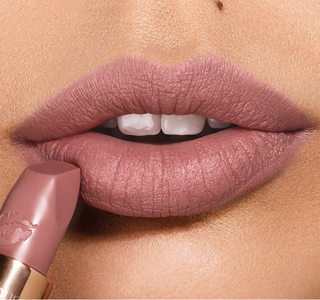 Lips close-up of a light-tone model applying a matte lipstick in a taupe nude shade,
