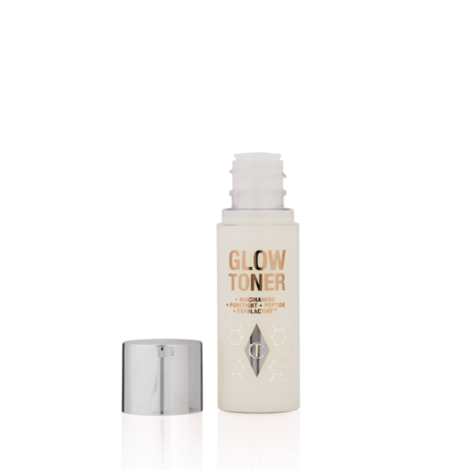 An open, travel-size, clear bottle filled with luminous, cream-coloured watery toner with its silver-coloured lid next to it.