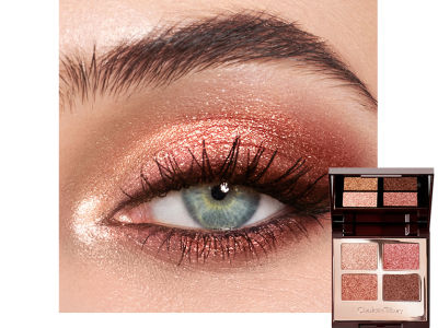 Close-up of a blue eye with shimmery copper, champagne, and brown eye makeup along with an open, mirrored-lid, quad eyeshadow palette with shimmery copper, champagne, and brown shades.