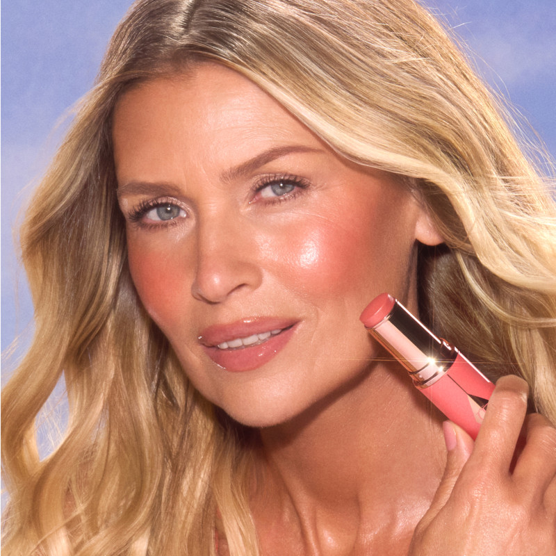 Model wears Unreal Blush Healthy Glow Stick in Peachy Glow