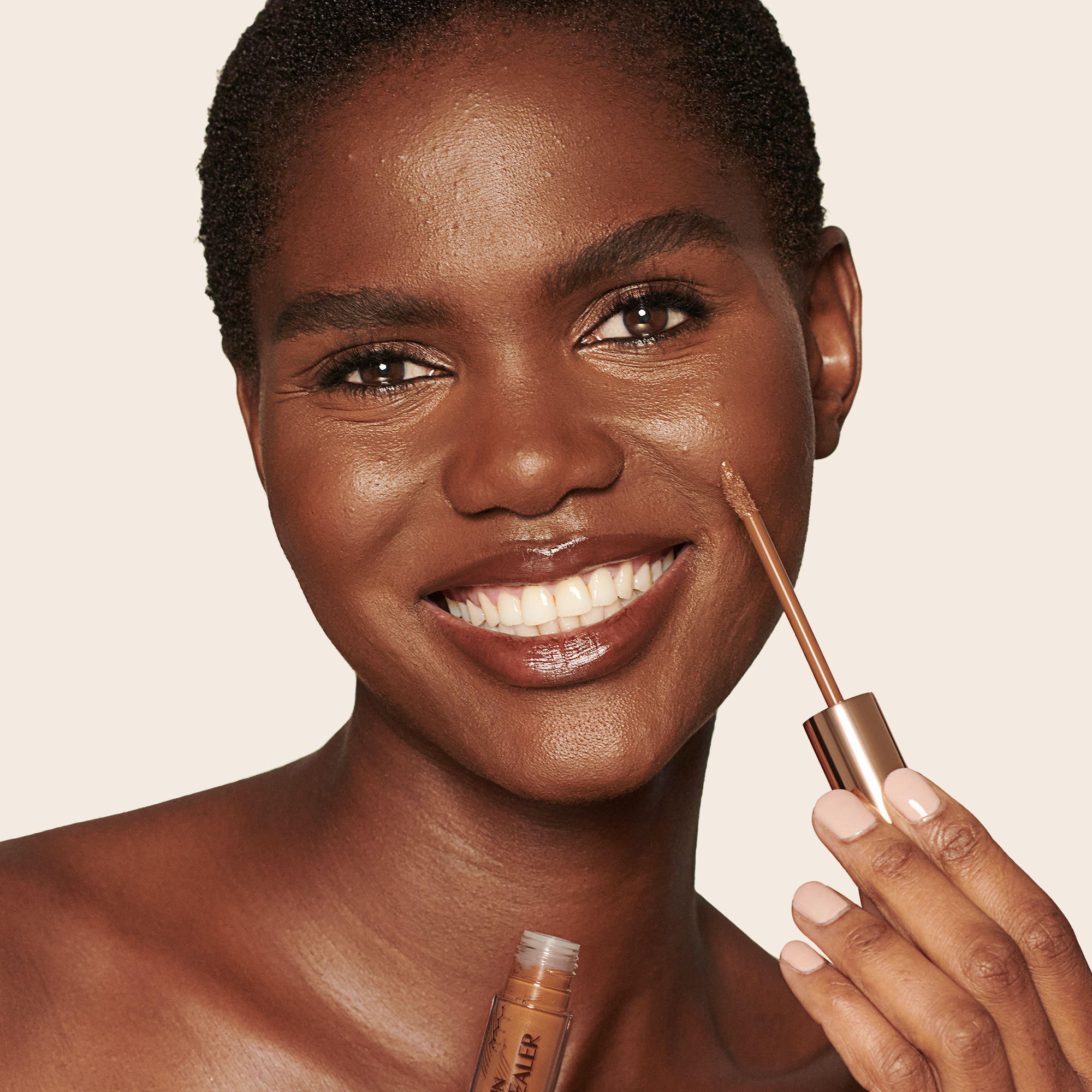 Deep-tone model with brown eyes wearing a radiant, concealer that brightens, covers blemishes, and makes her skin look fresh along with nude lip gloss and subtle eye makeup.