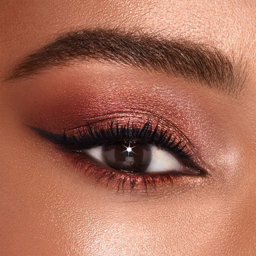 Primer plano de un solo ojo de una modelo de ojos marrones con sombra de ojos oro rosa brillante y marrón ahumado. 