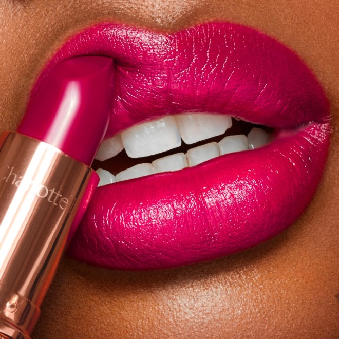 Lips close-up of a deep-tone model applying a bright fuchsia moisturising lipstick with a satin finish.