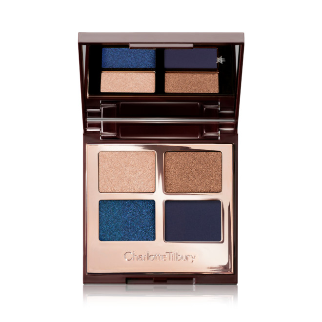 An opened eyeshadow palette with a mirror on the inside and four different matte and sparkly eyeshadows in royal blue, navy, champagne, and bronze. 