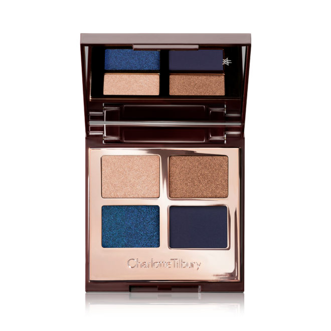 An opened eyeshadow palette with a mirror on the inside and four different matte and sparkly eyeshadows in royal blue, navy, champagne, and bronze. 