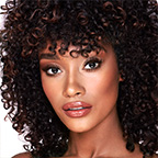 A deep-tone model with brown eyes wearing smokey brown eye makeup with warm bronze and pink blush, and glossy terracotta lips.