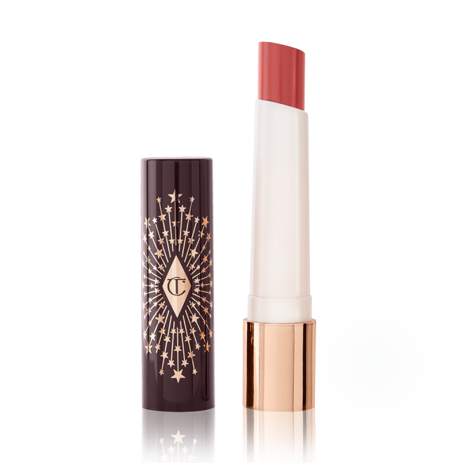 An open lipstick lip balm in a glossy soft coral shade, in white and gold tube with a black-coloured lid with gold sparkles all over it.