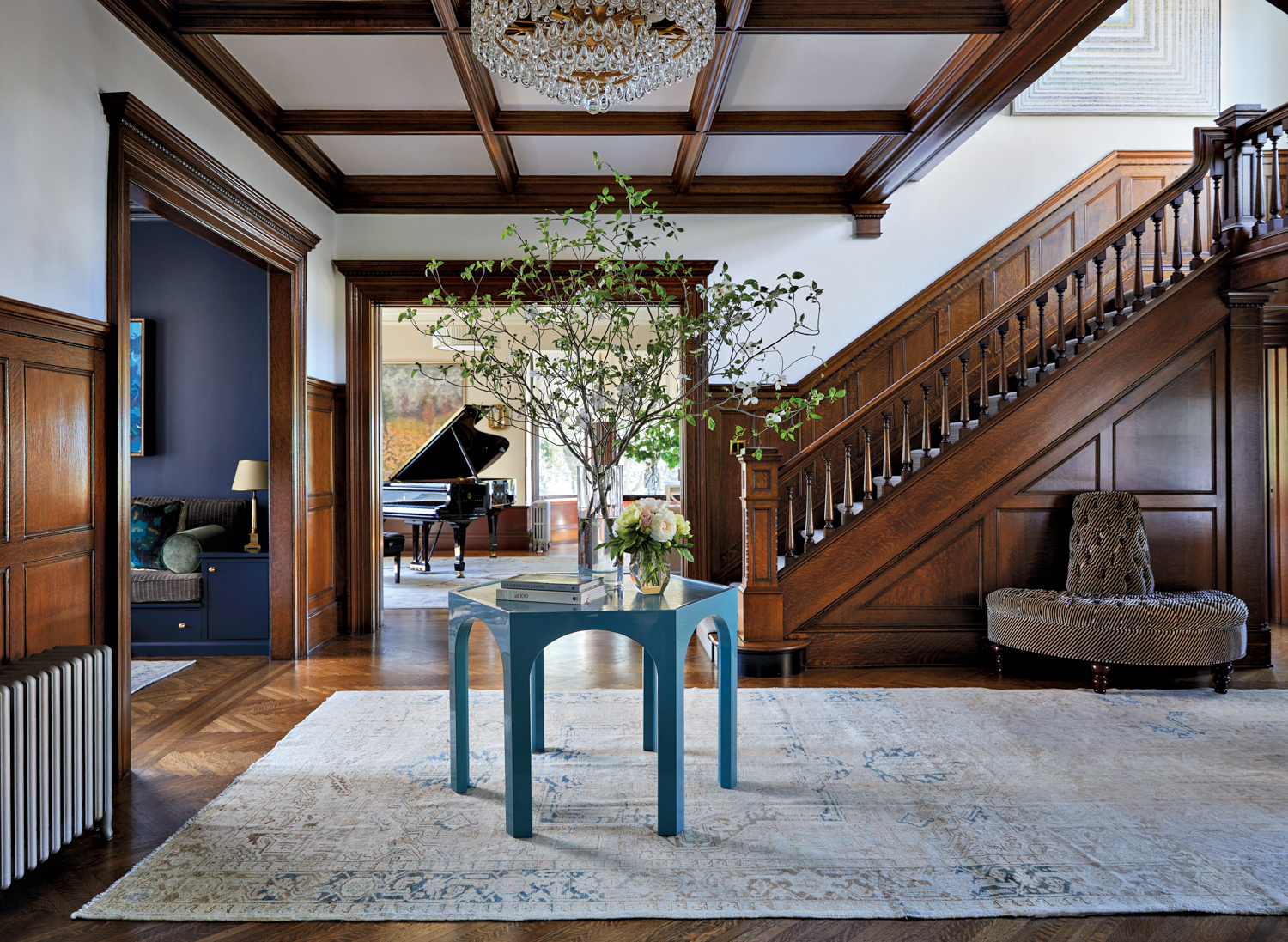 Foyer with dark wood paneling paired with a blue table and crystal chandelier.