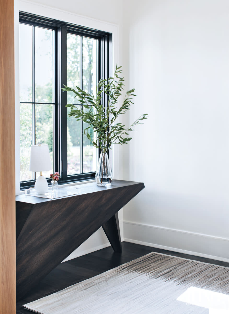 An angular dark wood console with flowers on top of it.