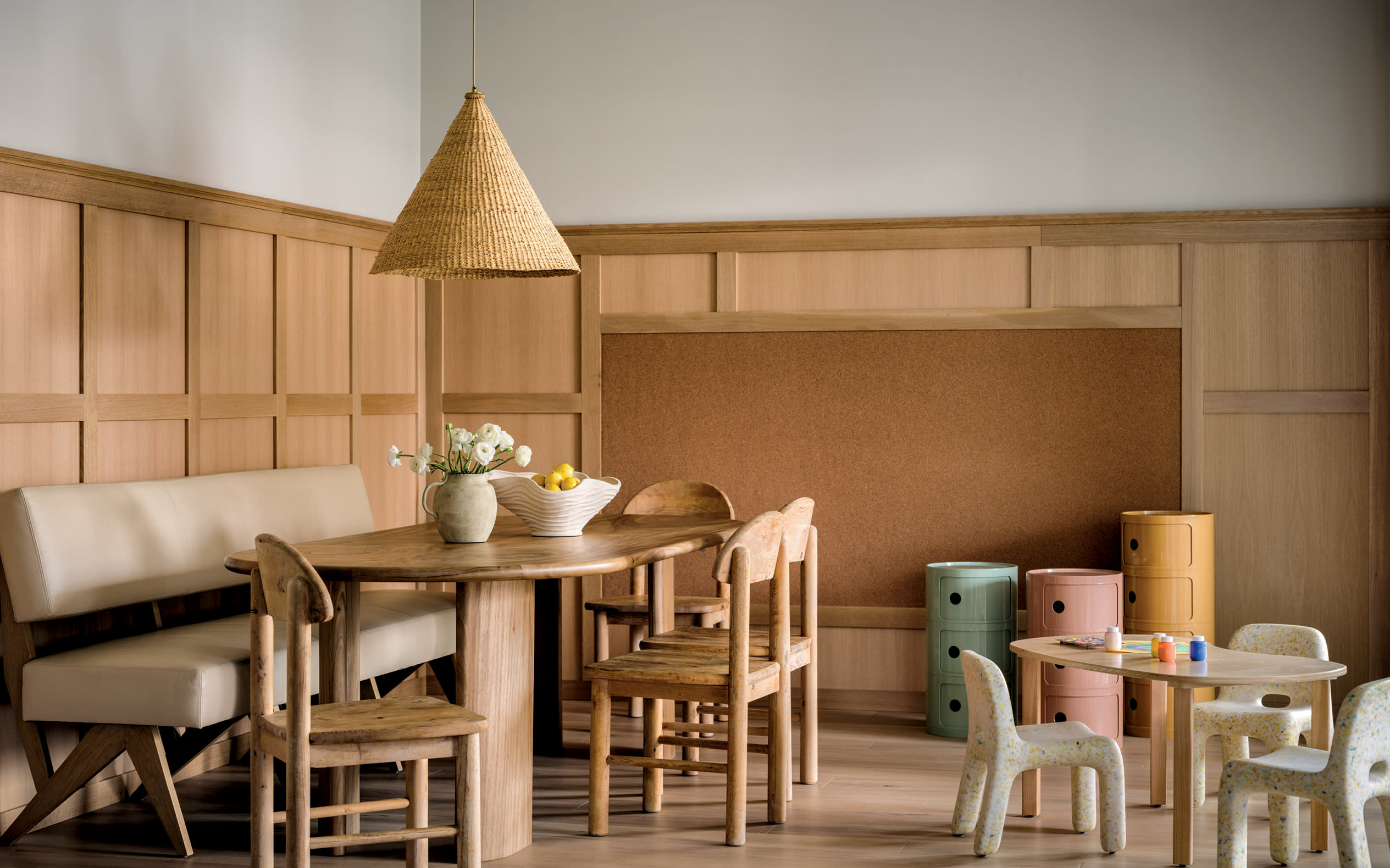 a triangular pendant light hangs above a light wood-colored breakfast nook next to a childrens table