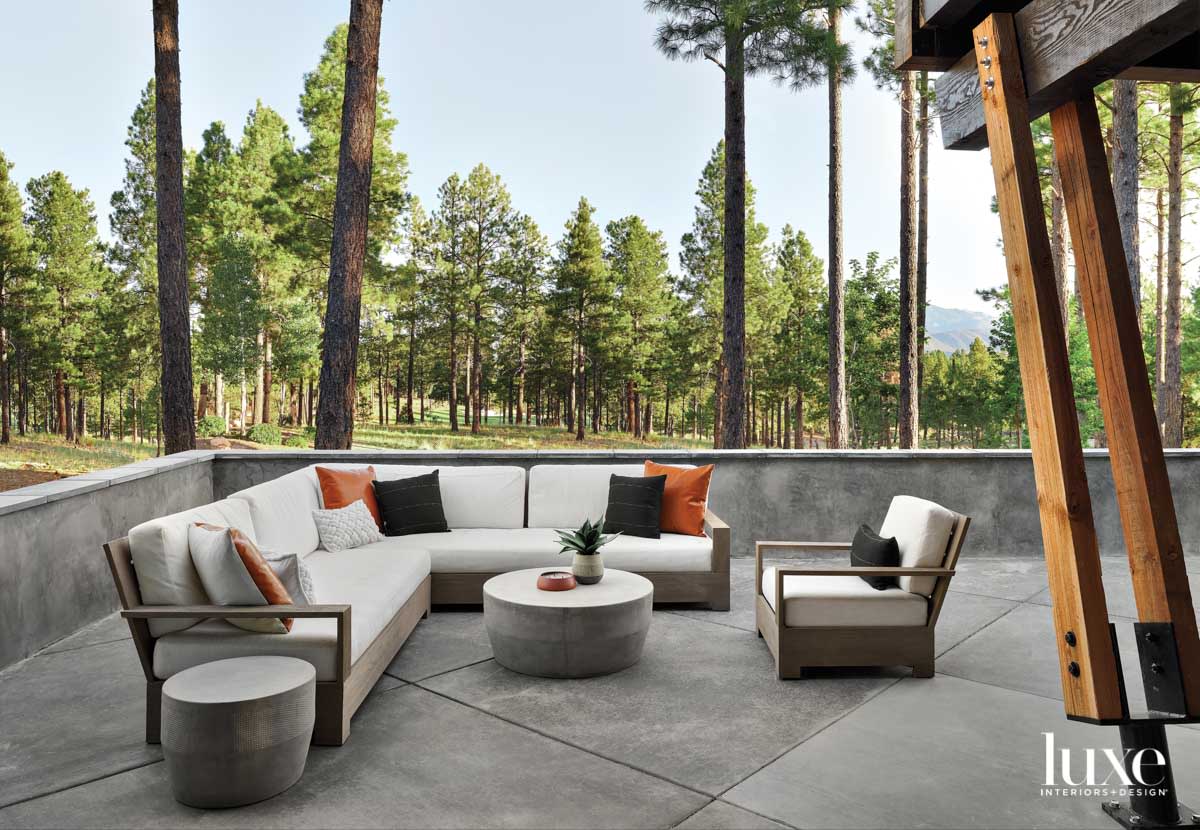 A patio with a chair, sectional and concrete coffee table. Woods are in the background.