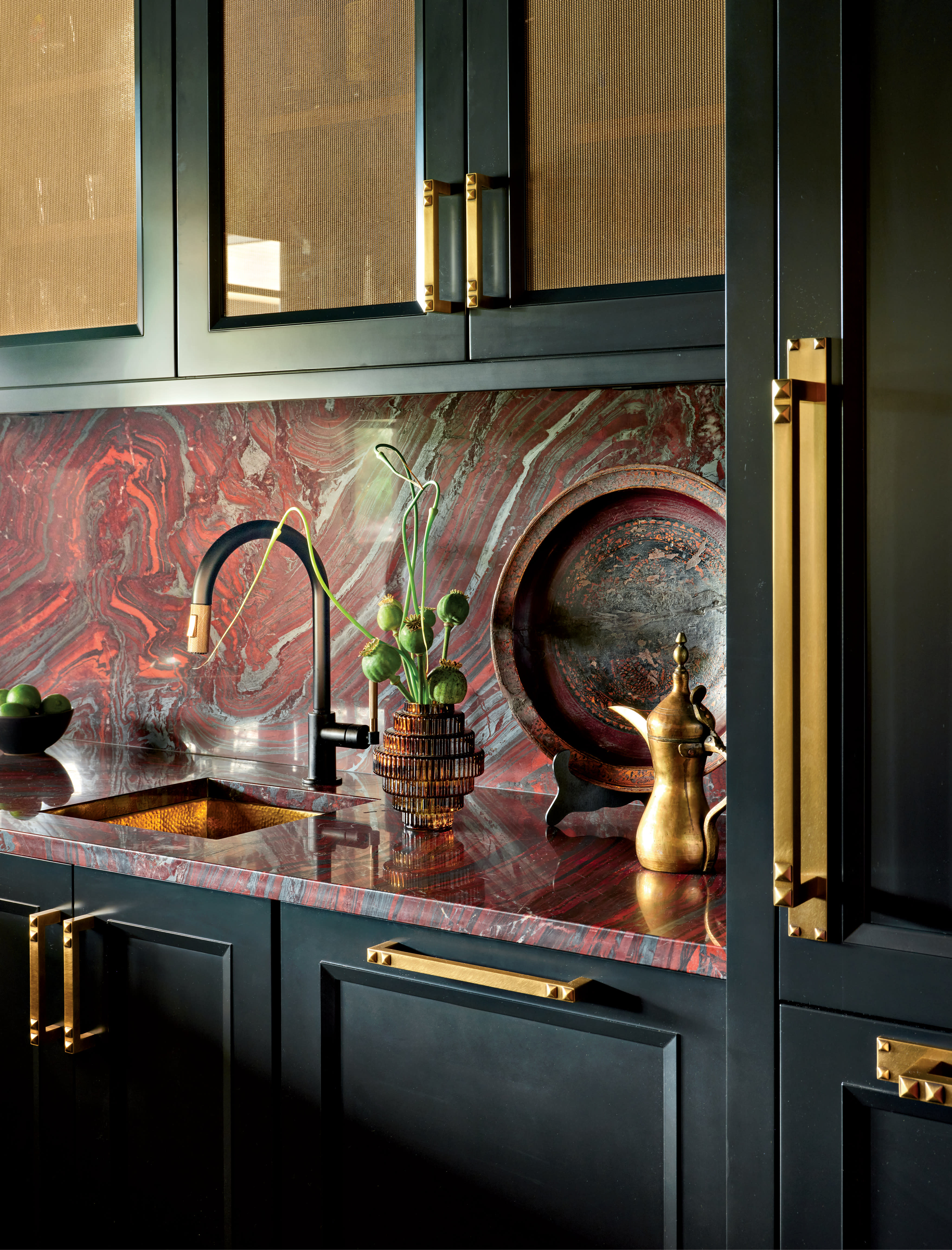 Elegant kitchen with a red marble backsplash, black and gold faucet, dark cabinets, brass accents, and decorative items. Luxurious and modern.