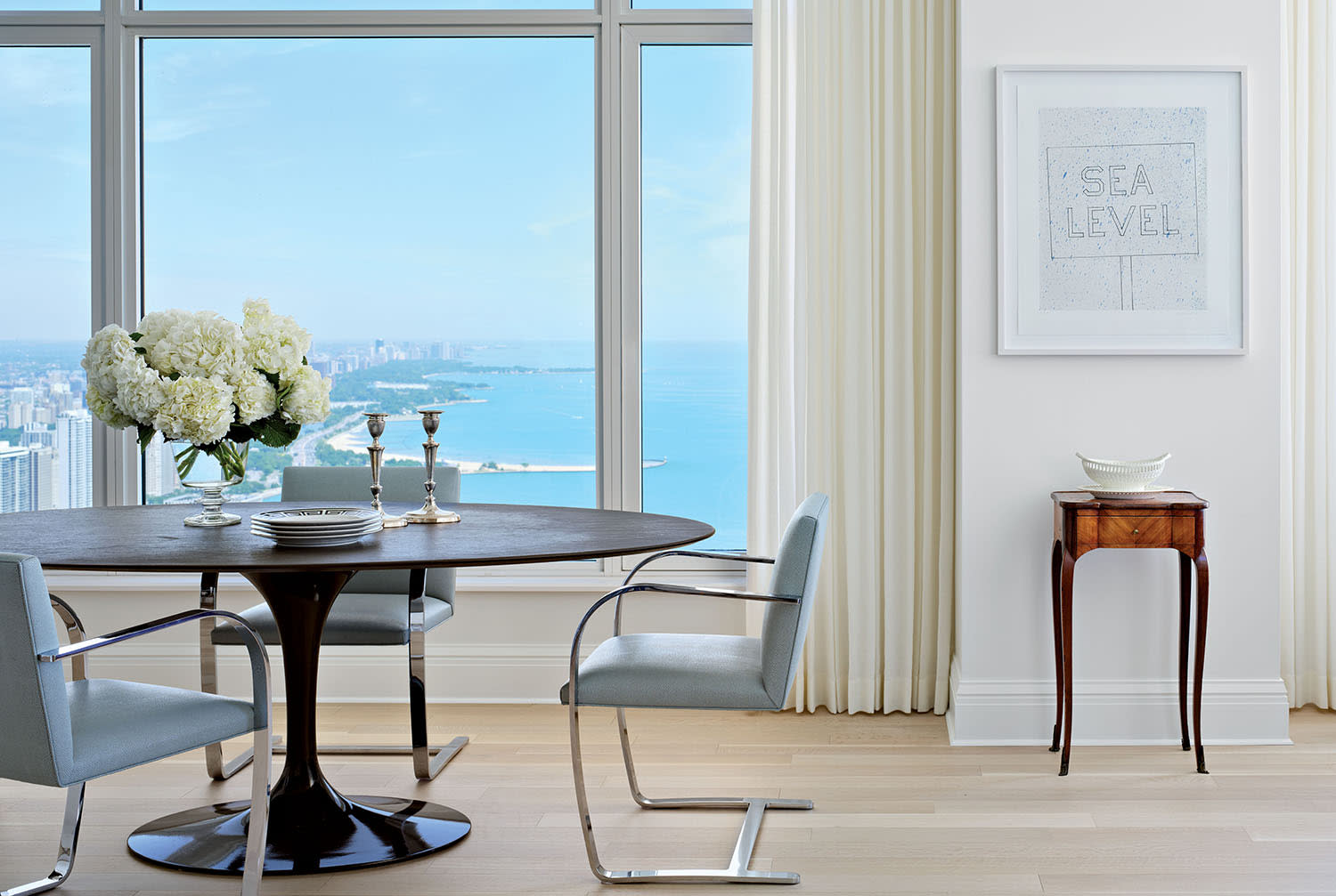 A dining table set with flowers and a pair of candlesticks, next to a bay window with lake views.
