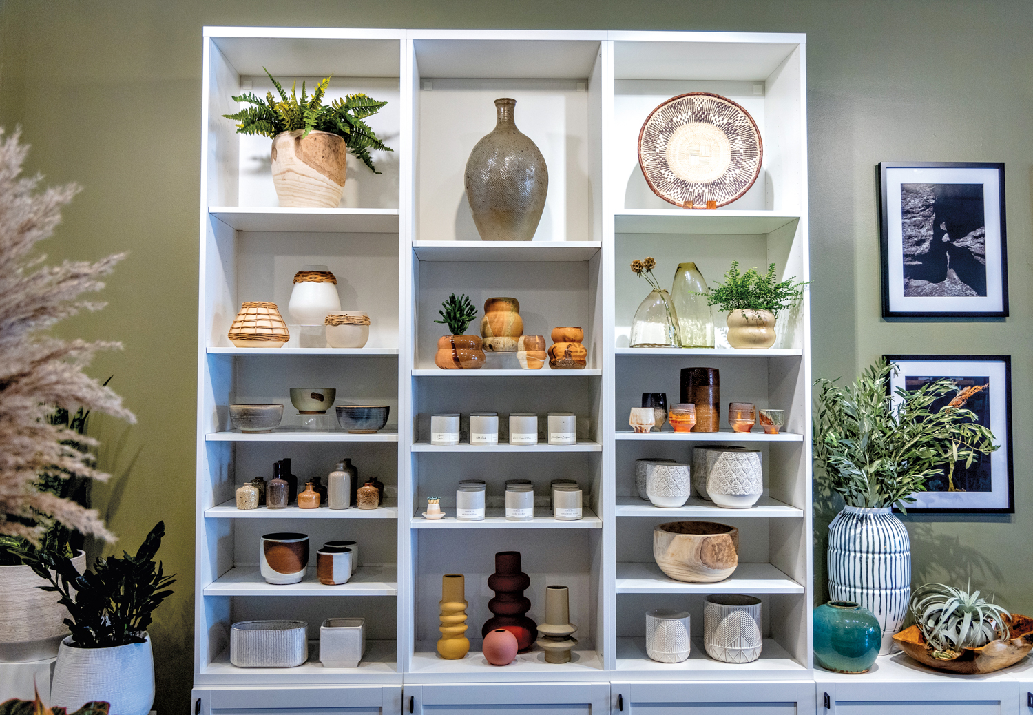 White shelf full of various vases, cups, bowls and plants