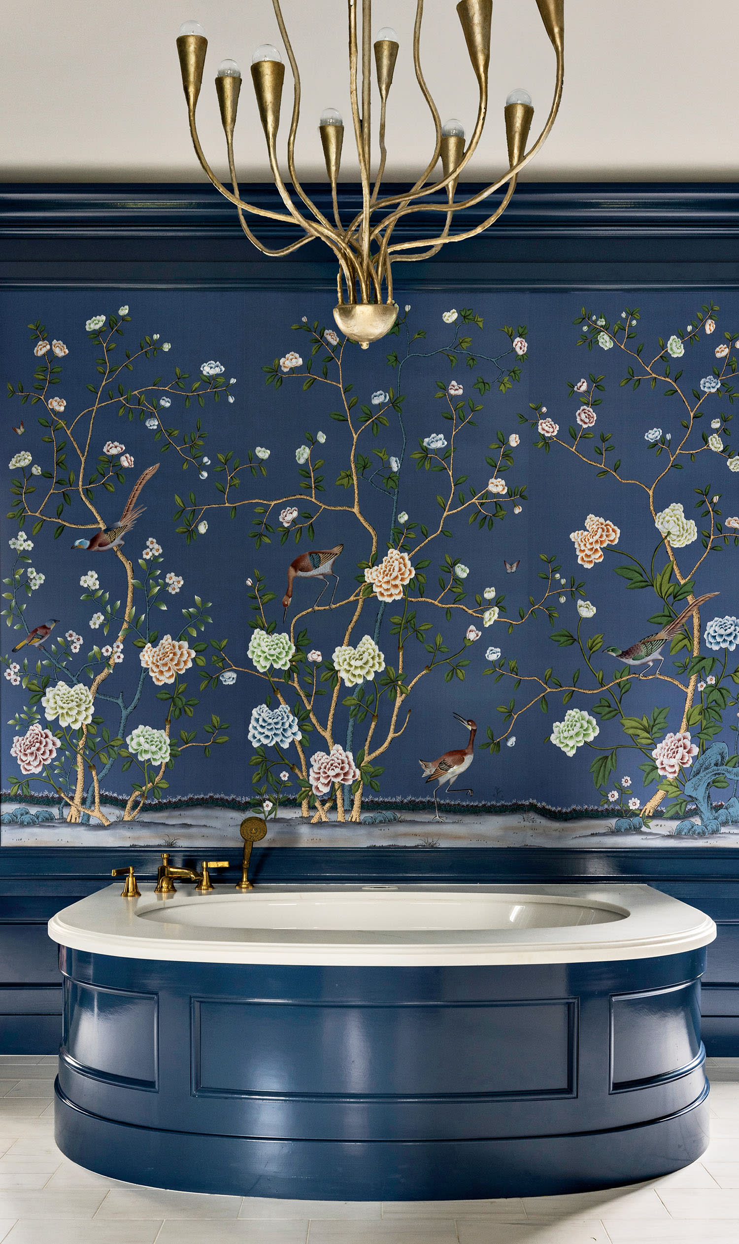 Luxurious bathroom with navy paneling, featuring an ornate floral and bird wallpaper in elegant colors. A central golden chandelier adds sophistication.