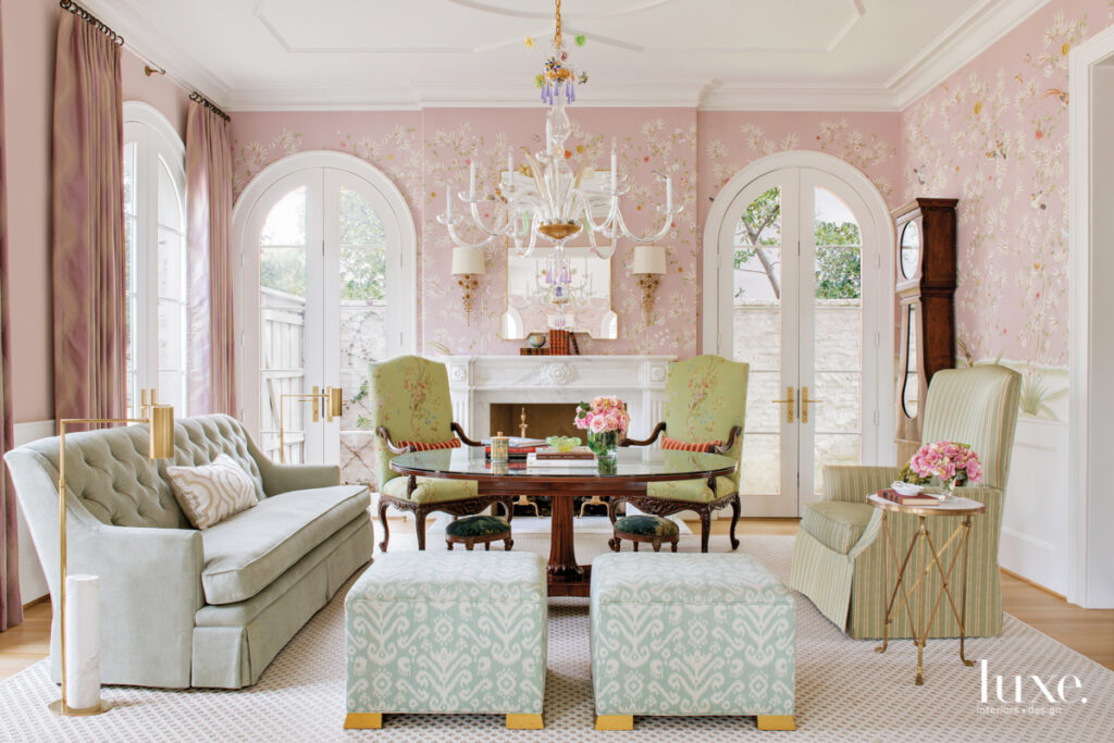 Brunschwig & Fils wallpaper from Lee Jofa and a Thomas Grant custom chandelier make for a spirited yet classic formal living room. Kravet fabric covers the custom sofa and twin ottomans, while matching antique chairs wear ScalamandreÌ. A center table from Legacy Antiques and 19th-century French clock from Pittet Architecturals contribute to an evolved-over-time feel.