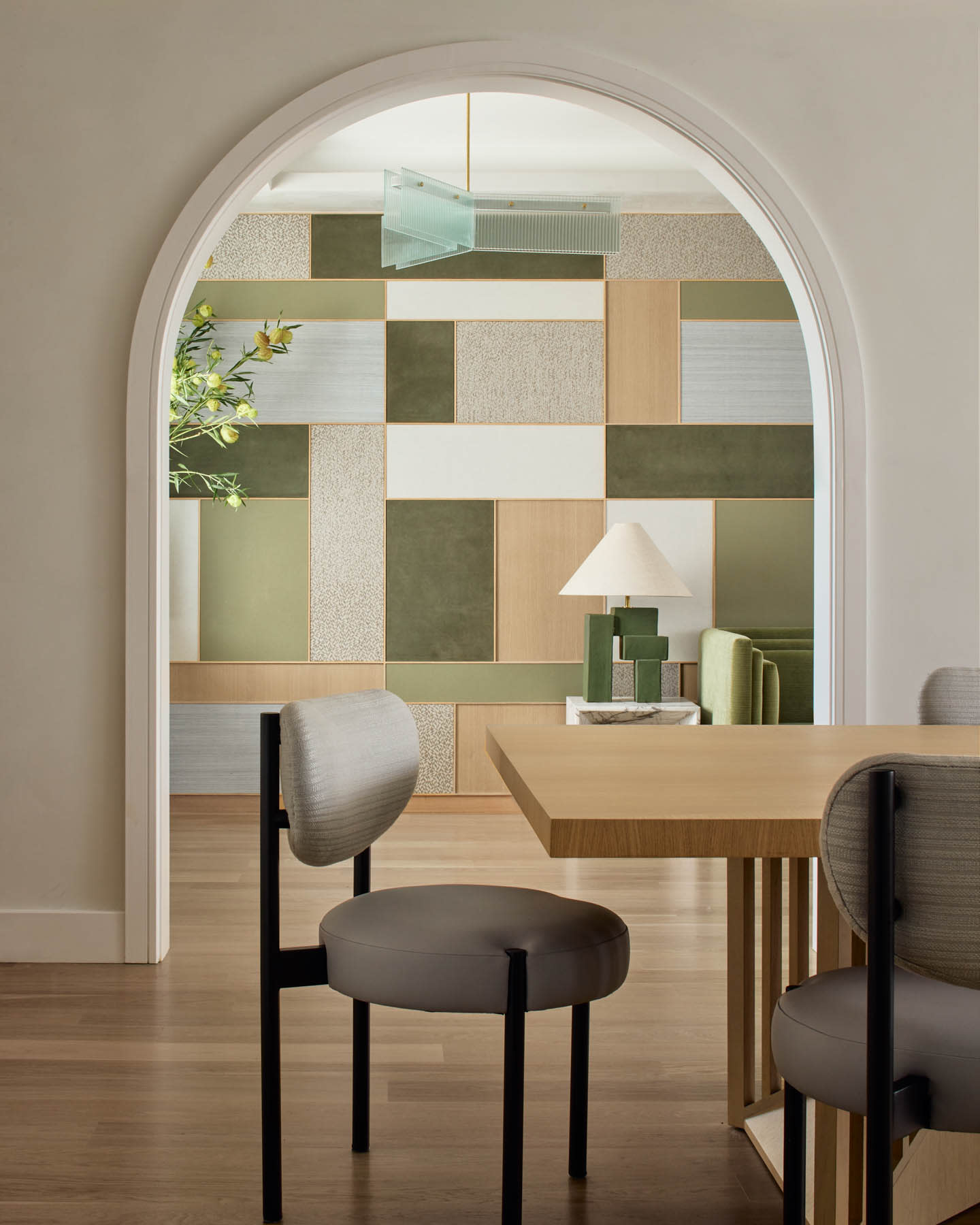 Modern interior with an arched doorway framing a geometric accent wall in green, beige, and white. Minimalist furniture, soft tones, calm ambiance.