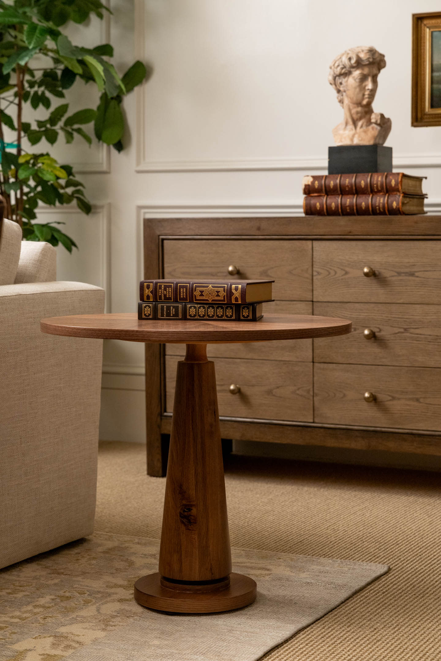 A cozy living room with a wooden side table holding stacked hardcover books, next to a beige sofa.