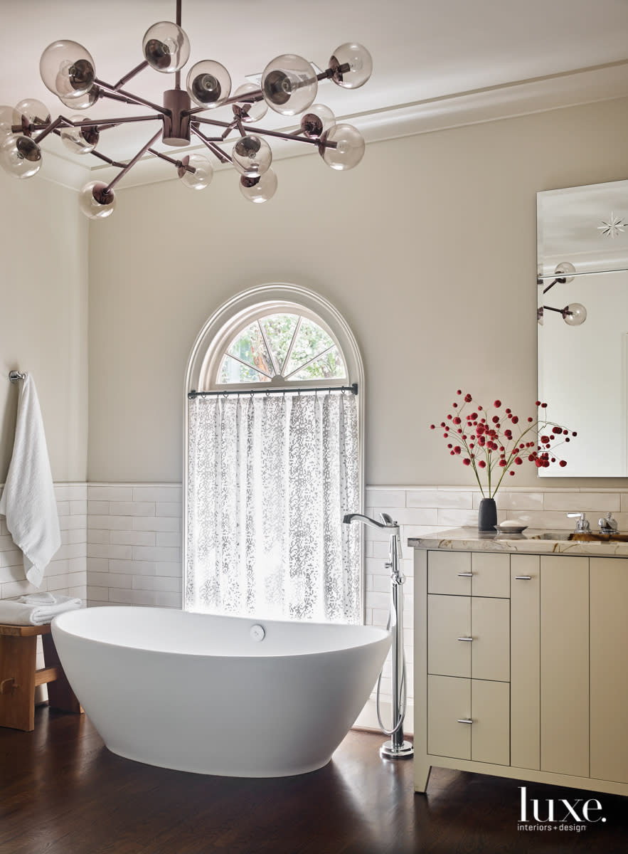 neutral bathroom with elliptical soaking tub, modern chandelier and traditional cabinetry