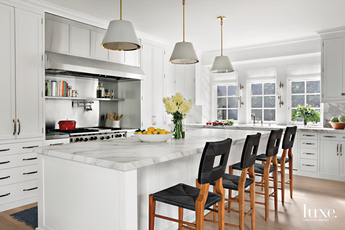 All-white kitchen with marble island and black barstools.