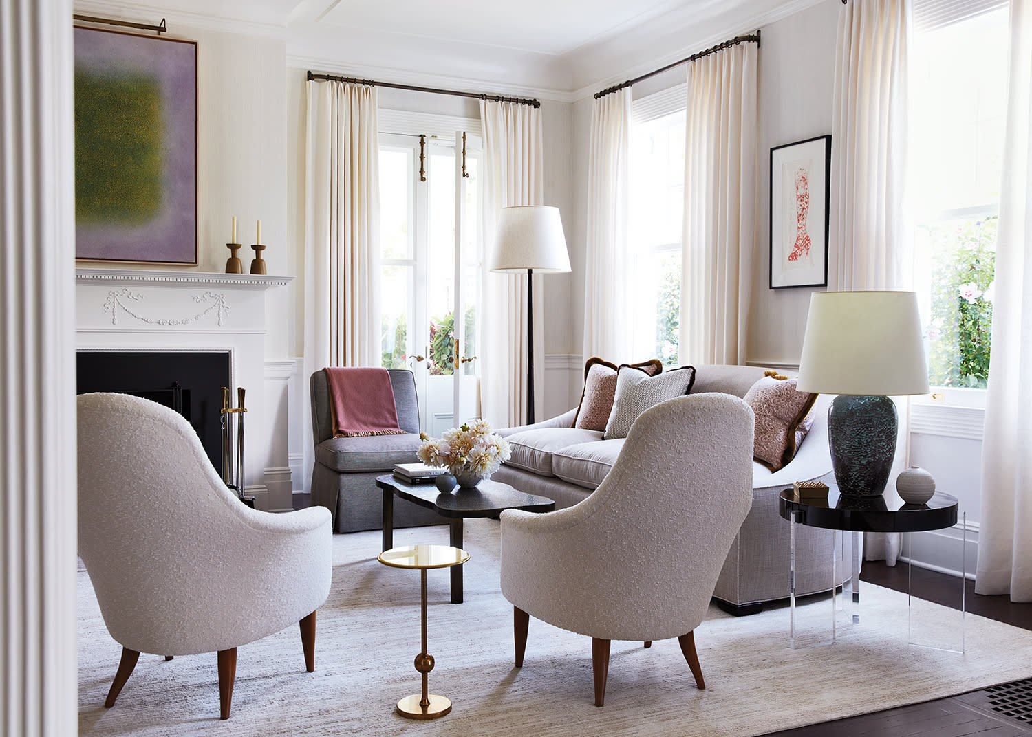 Elegant living room with cream armchairs, light gray sofa, and large windows with curtains. A fireplace, modern art, and lamps create a cozy atmosphere.