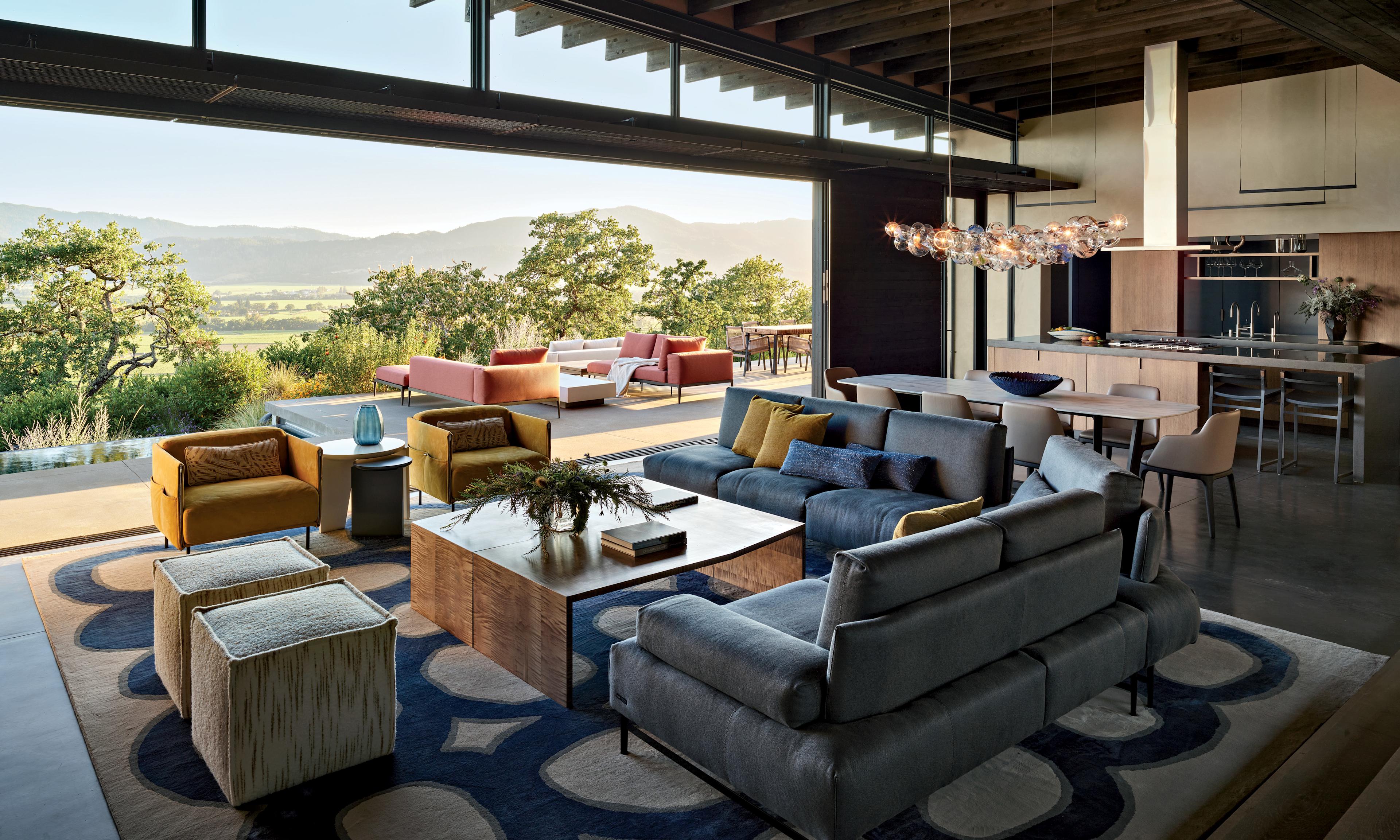 A living room space decorated with colorful ottomans, a sectional couch and armchairs and a side table.