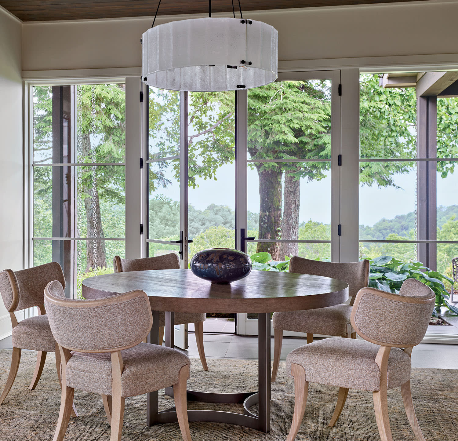 A round table and chairs sit under a chandelier, positioned near glass doors.