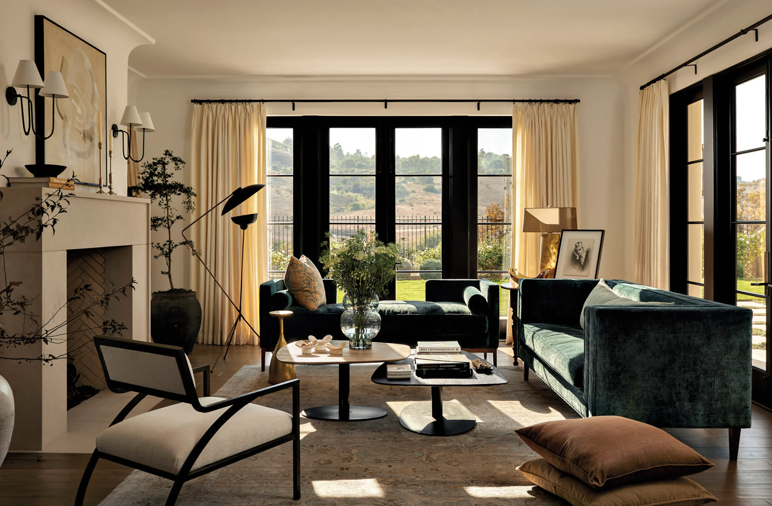 living area with green velvet sofas, coffee tables, sculptural floor lamp, fireplace, two stacked cushions and an armchair