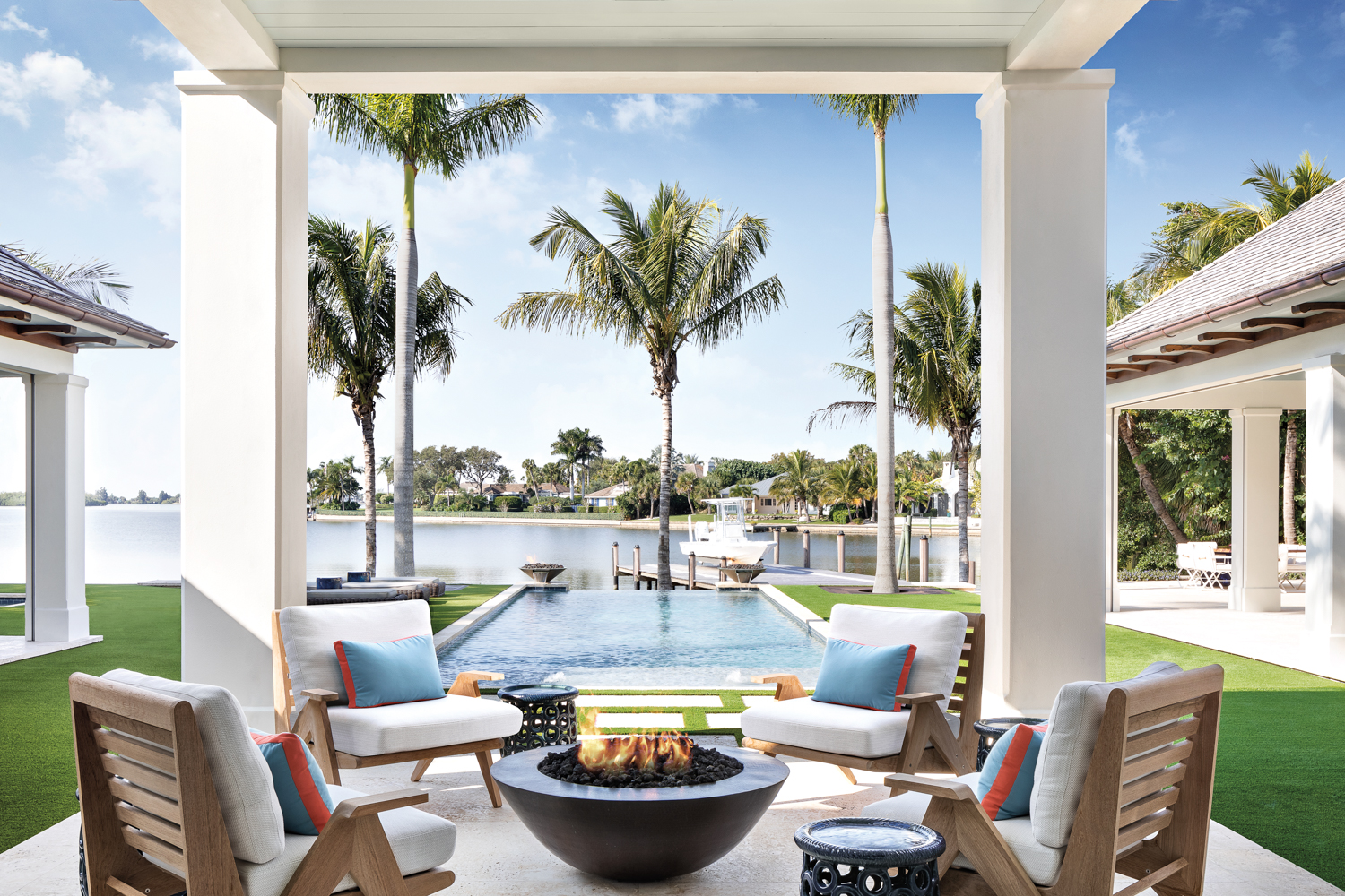 outdoor covered loggia with four armchairs, fire pit and view of pool and waterway