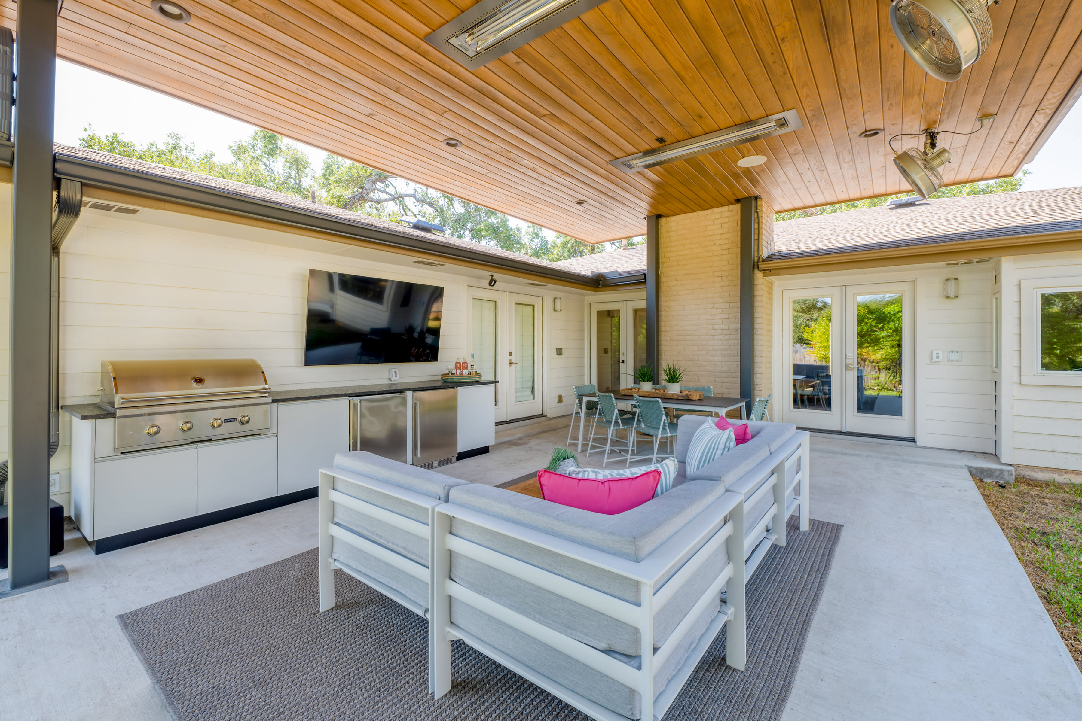 This modern patio features a sleek built-in grill, stainless
appliances, a TV, and a wood-paneled ceiling with heaters. Stylish seating, vibrant accents, and
an inviting dining area create the perfect space for year-round entertaining.