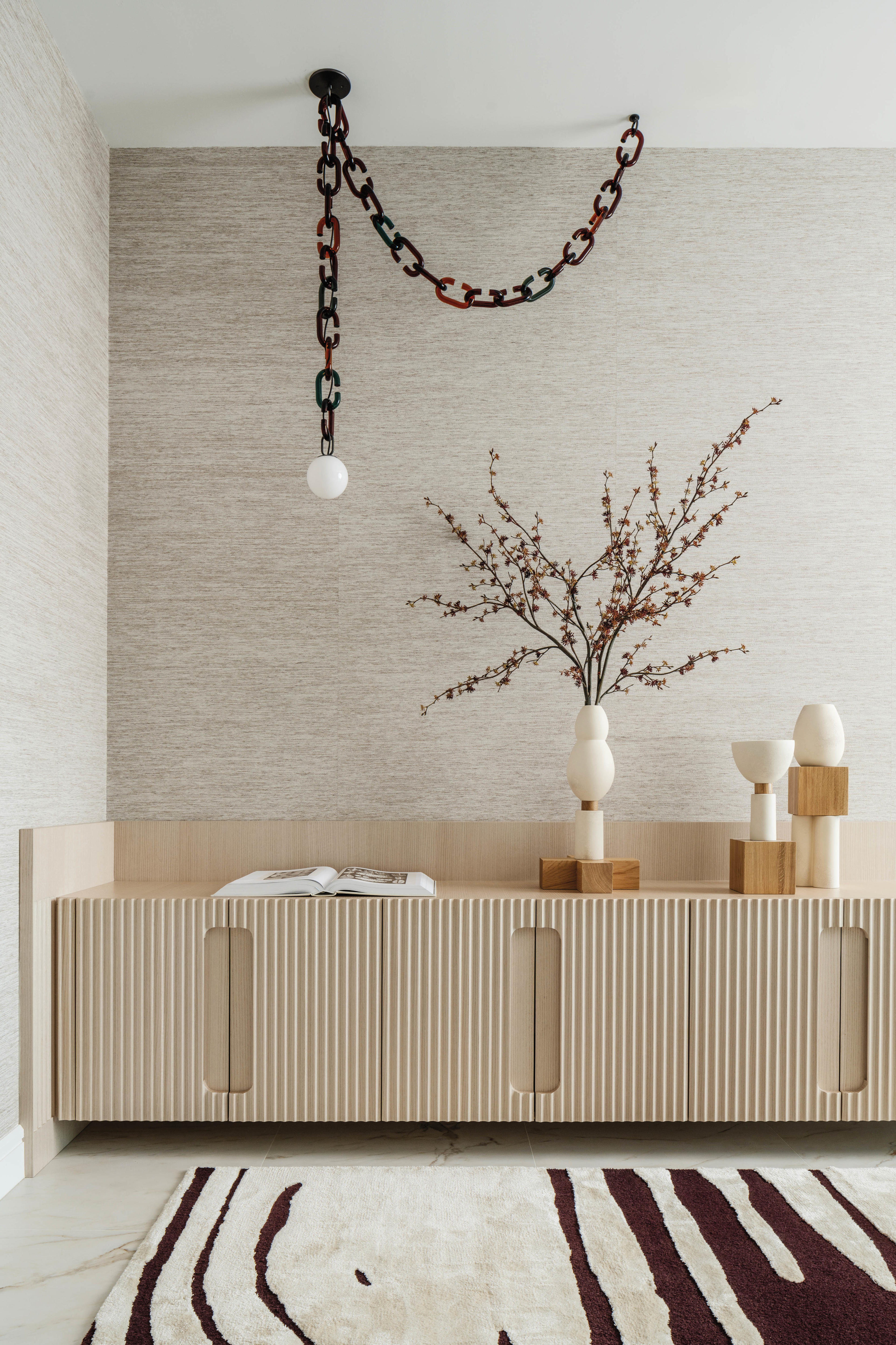 a light wash wood cabinet in a bedroom below a chain-like chandelier 