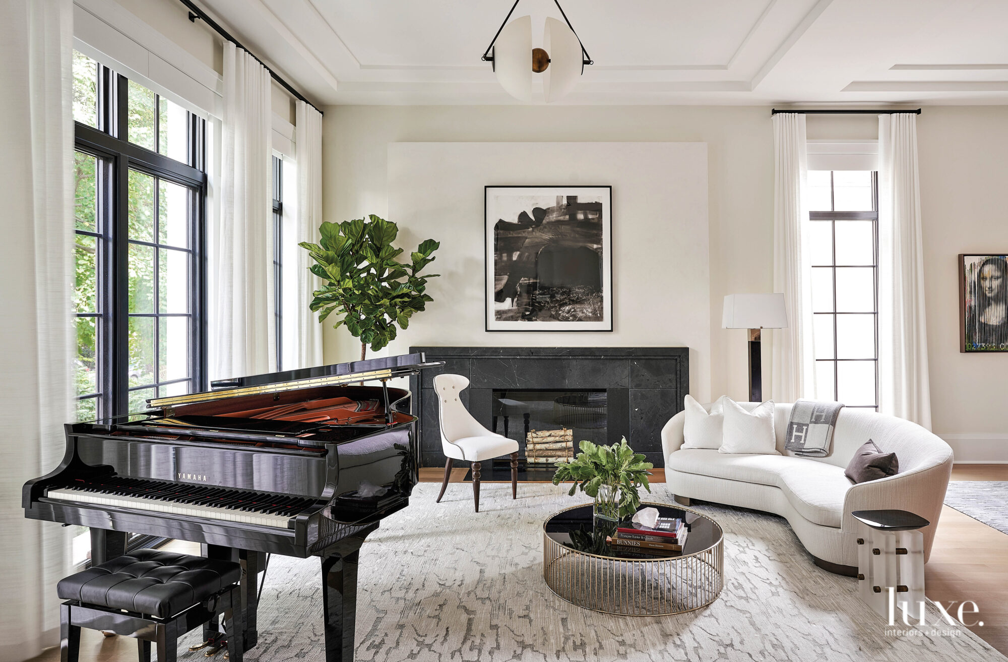 The living room has a a baby grand piano, a white curved sofa and black marble fireplace.