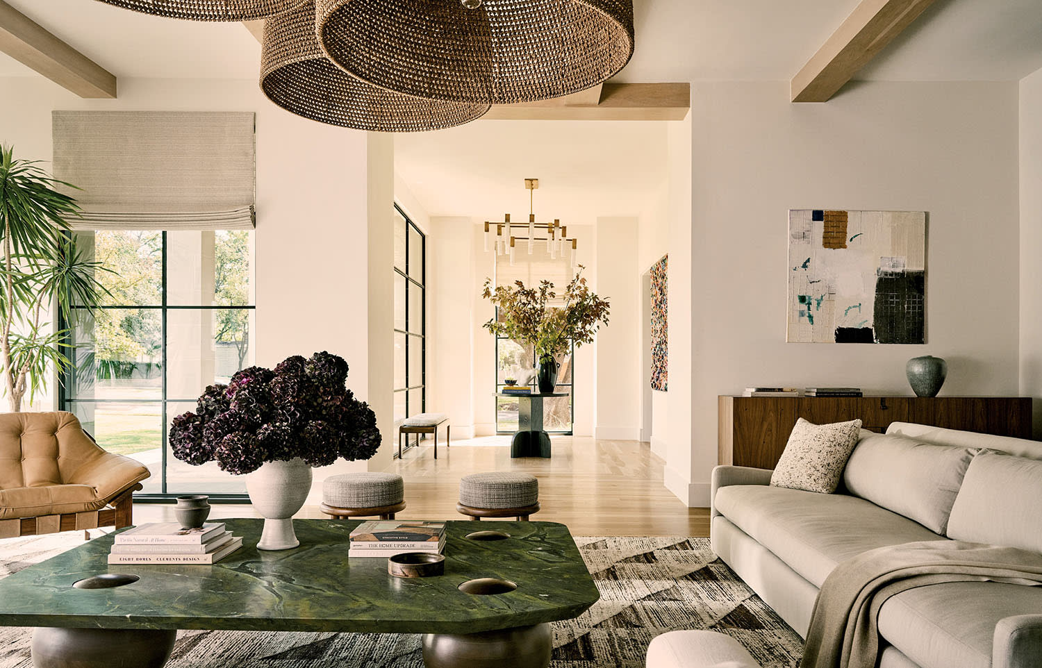 Contemporary living room with neutral tones, featuring a green marble coffee table, plush sofa, woven pendant lights, art, and large floral arrangement.