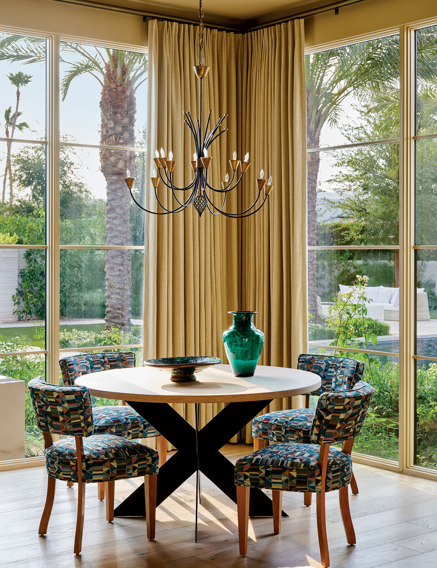A sunlit dining area with a round table and colorful patterned chairs. 