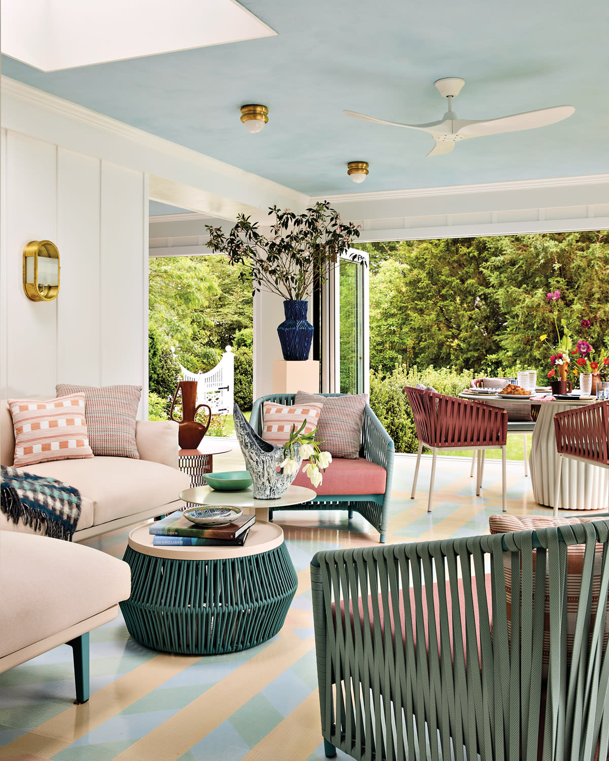 Stylish patio with pastel furniture under a light blue ceiling. Open view to lush garden. Cozy, inviting ambiance with modern decor and vibrant accents.