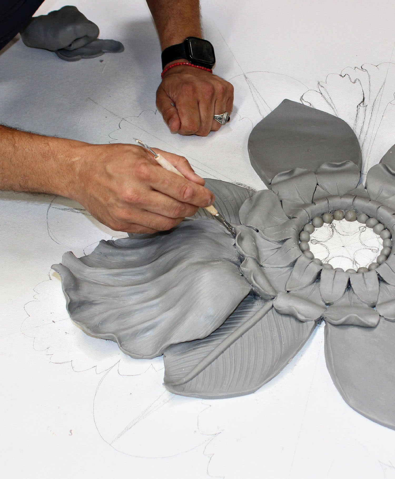 An artist carves intricate florals from clay