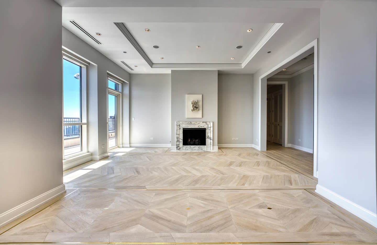 Spacious and elegant living room with light wood flooring, a marble-framed fireplace, and large windows offering vibrant natural light and city views.