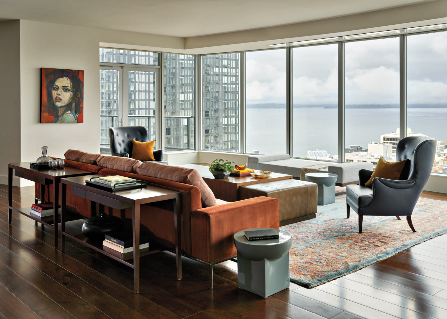 Living room with tan sofa and wingback chairs with windows looking out over downtown Seattle