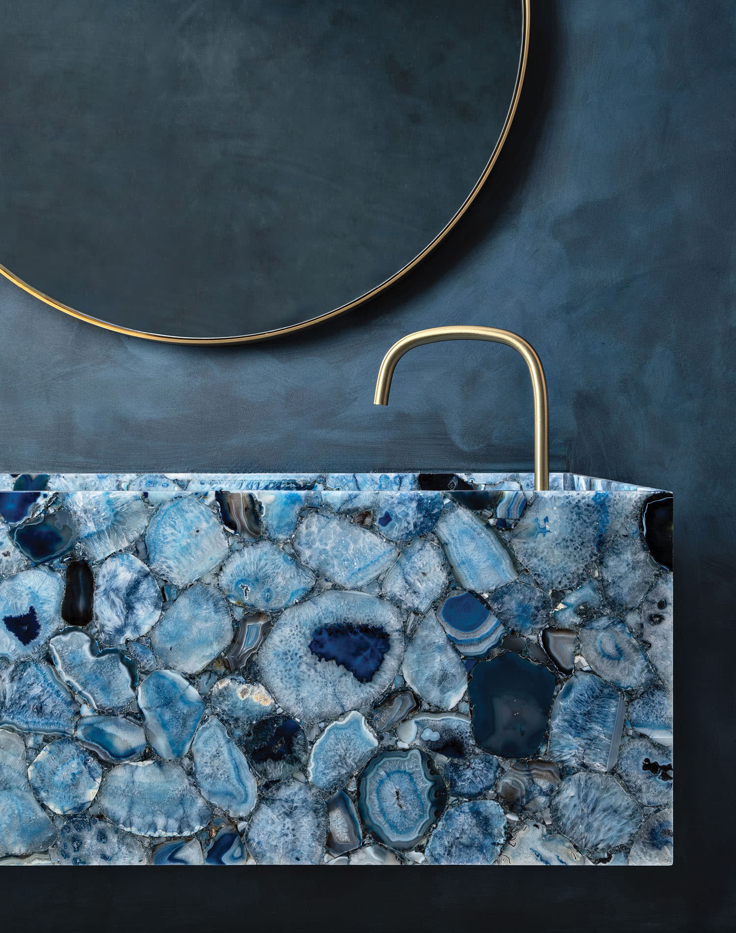 A vanity crafted with blue agate sits under a round mirror in a powder room.