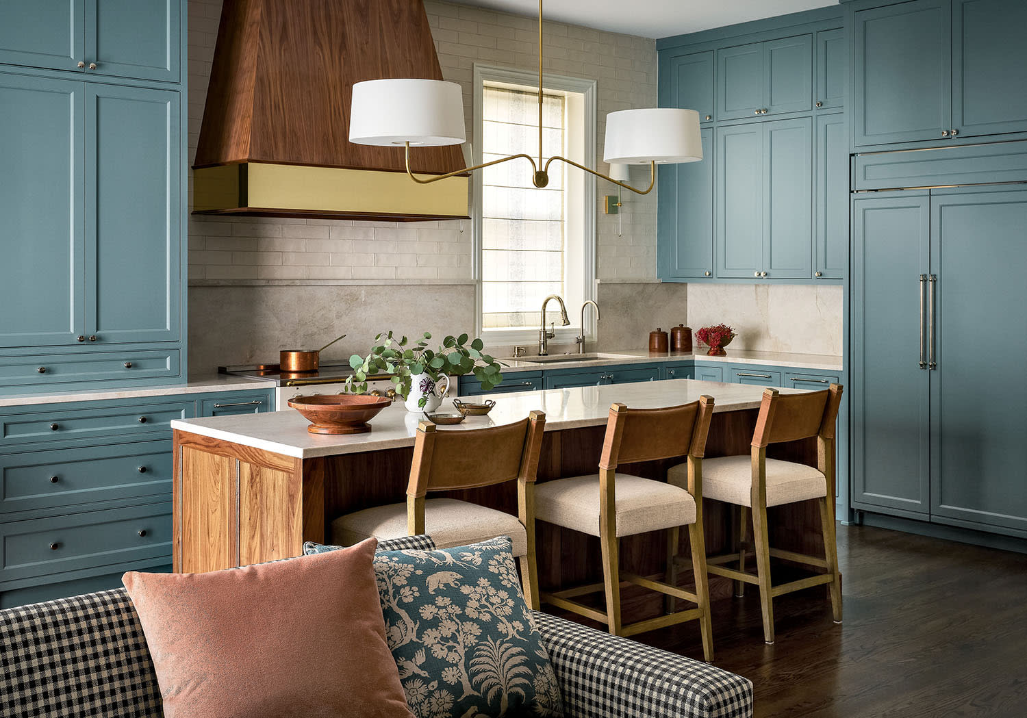 An island set with stools in a kitchen with blue cabinets and a white tile backsplash behind the stove.