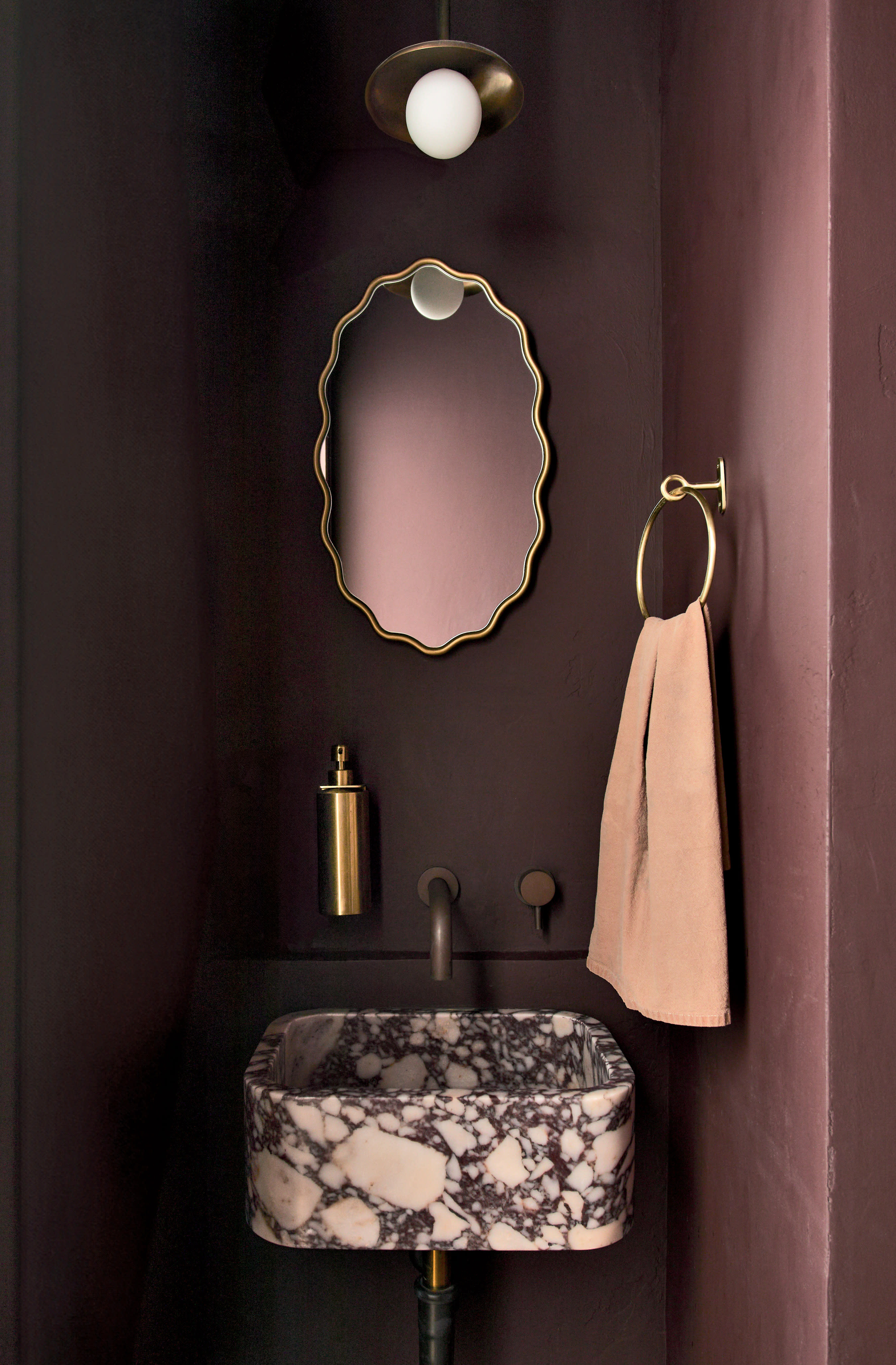 A bathroom with deep purple walls and a scalloped mirror mounted over the sink.