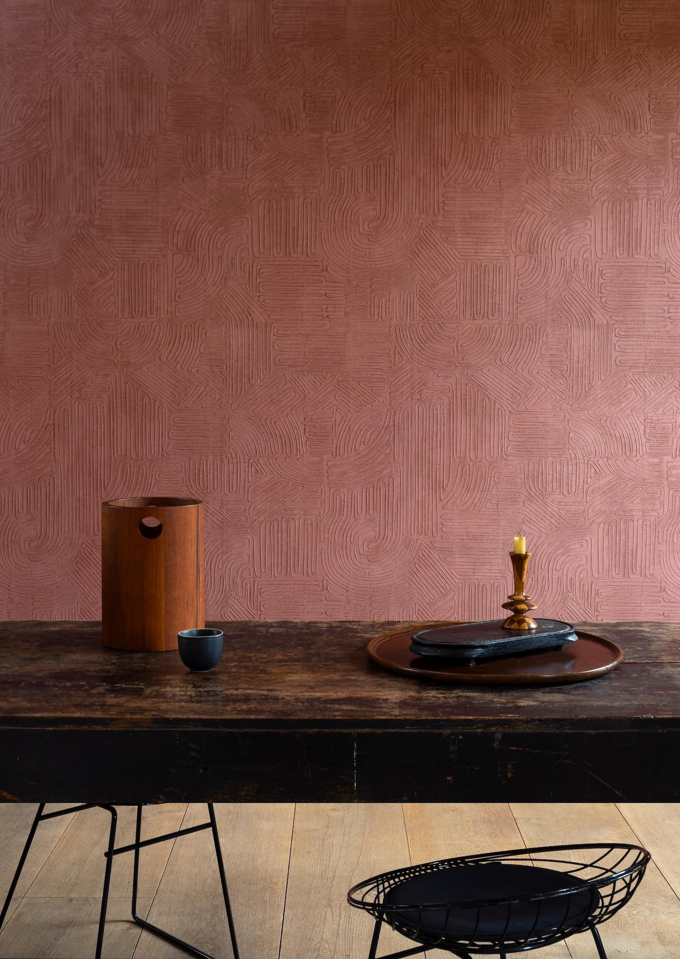 Warm-toned room with a textured reddish wall. A dark wood table holds a wooden vase, a small cup, and a tray with a candleholder. Calm, minimalist feel.