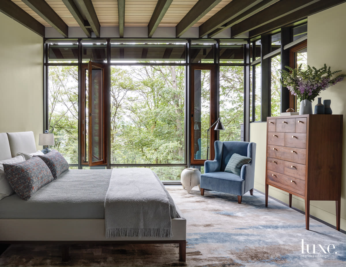 master bedroom with window walls and a blue corner chair