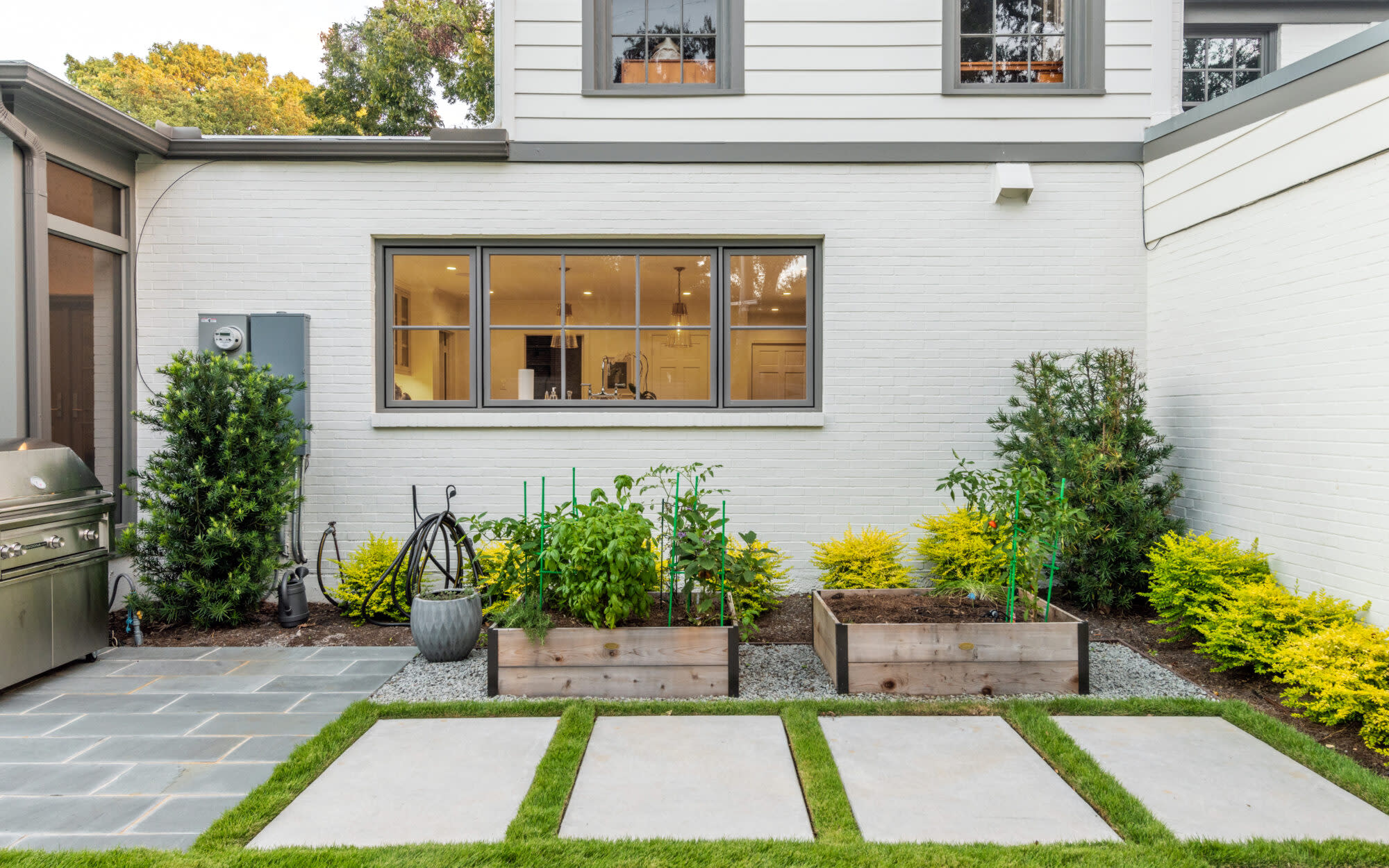 Raised garden beds and lawn path along a white modern farmhouse