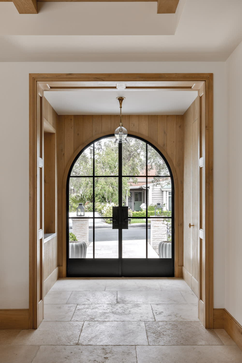 entrance with curved blackened steel and glass double door with light colored French oak panel walls and limestone flooring by Marie Carson