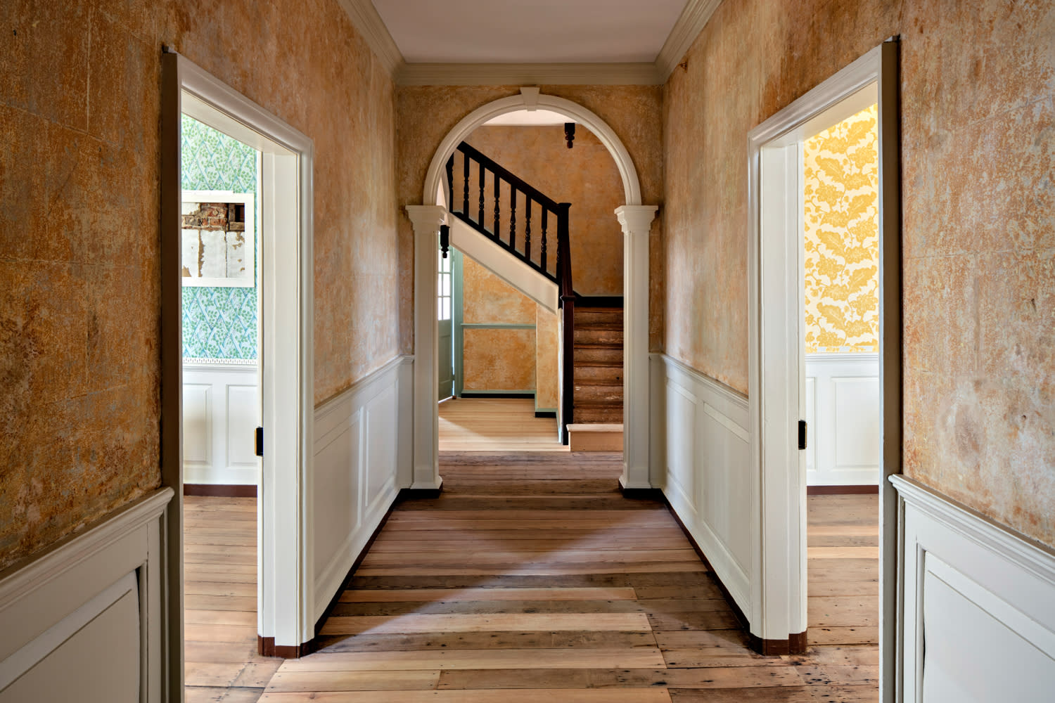 hallway of a historic home with an arched doorway leading toward the stairs