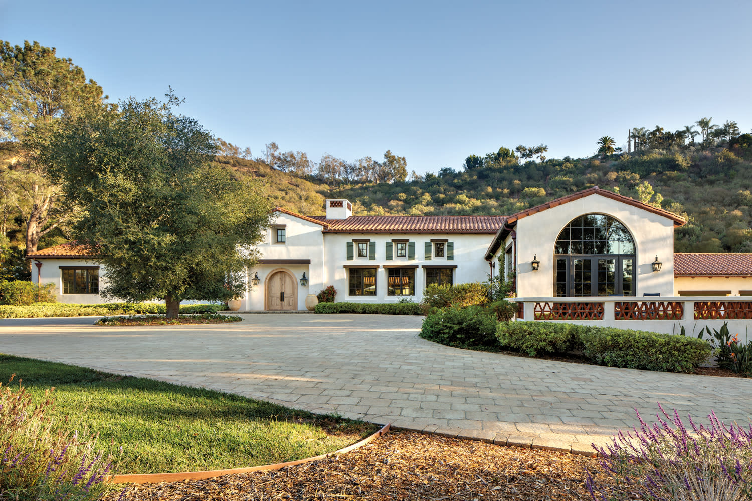 Exterior shot of entire Mediterranean-style, one-level home with a hill in the back