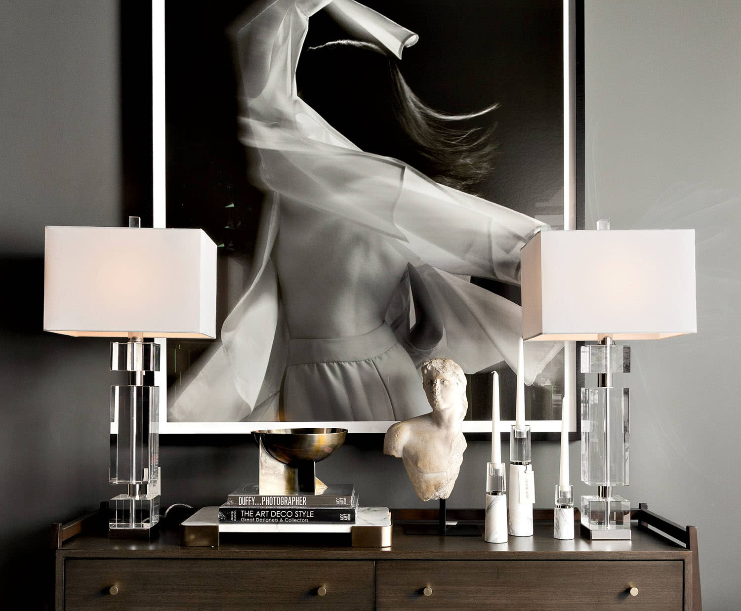 A dresser with lamps and books sits under a framed black and white photograph.