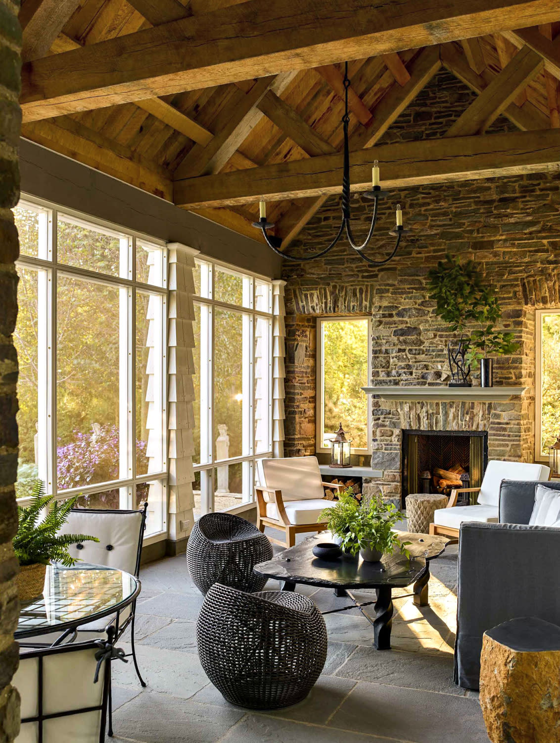 A spacious indoor-outdoor living room featuring a prominent stone fireplace as the focal point.