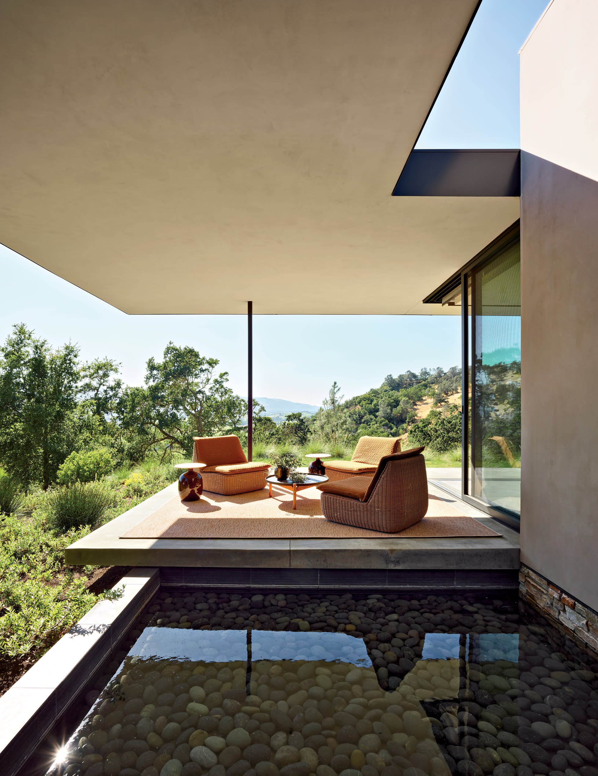 A small outdoor area with three chairs and side tables sits under an awning next to a small pond.